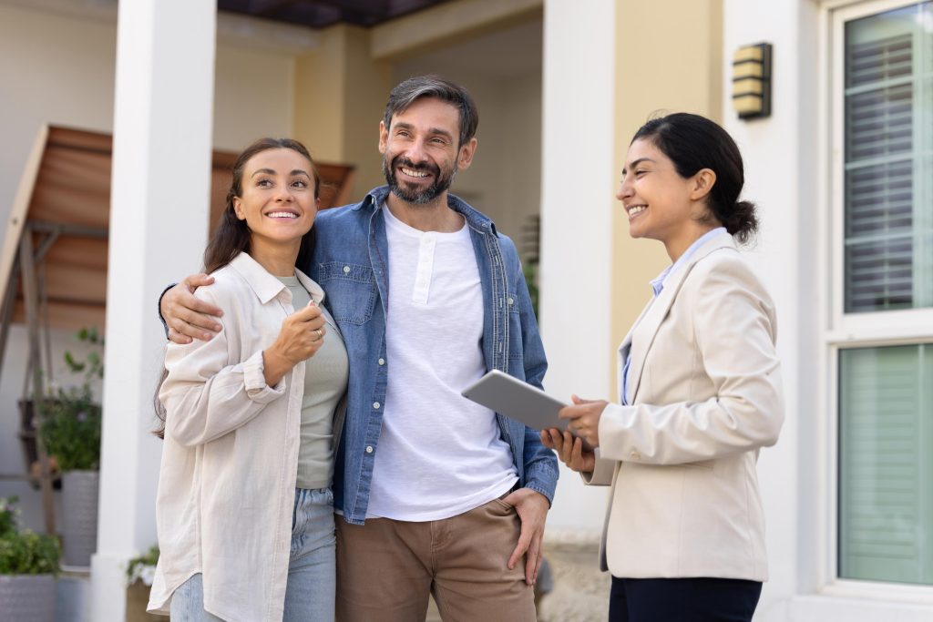 Casal feliz com corretora sorridente discutindo compra de imóvel no novo bairro.