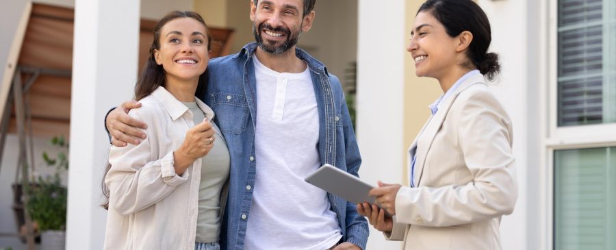 Casal feliz com corretora sorridente discutindo compra de imóvel no novo bairro.