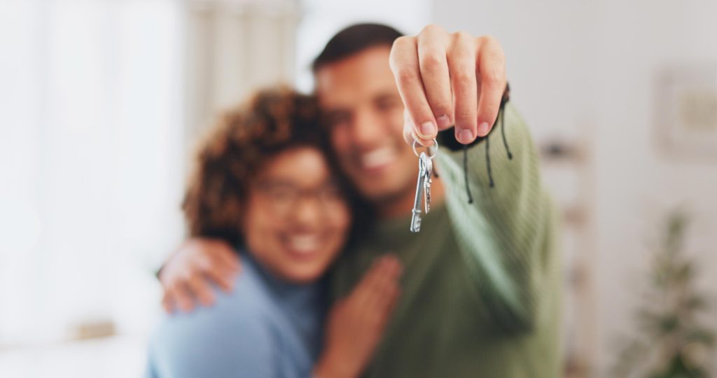 Casal sorridente segurando as chaves do novo apartamento após a compra.