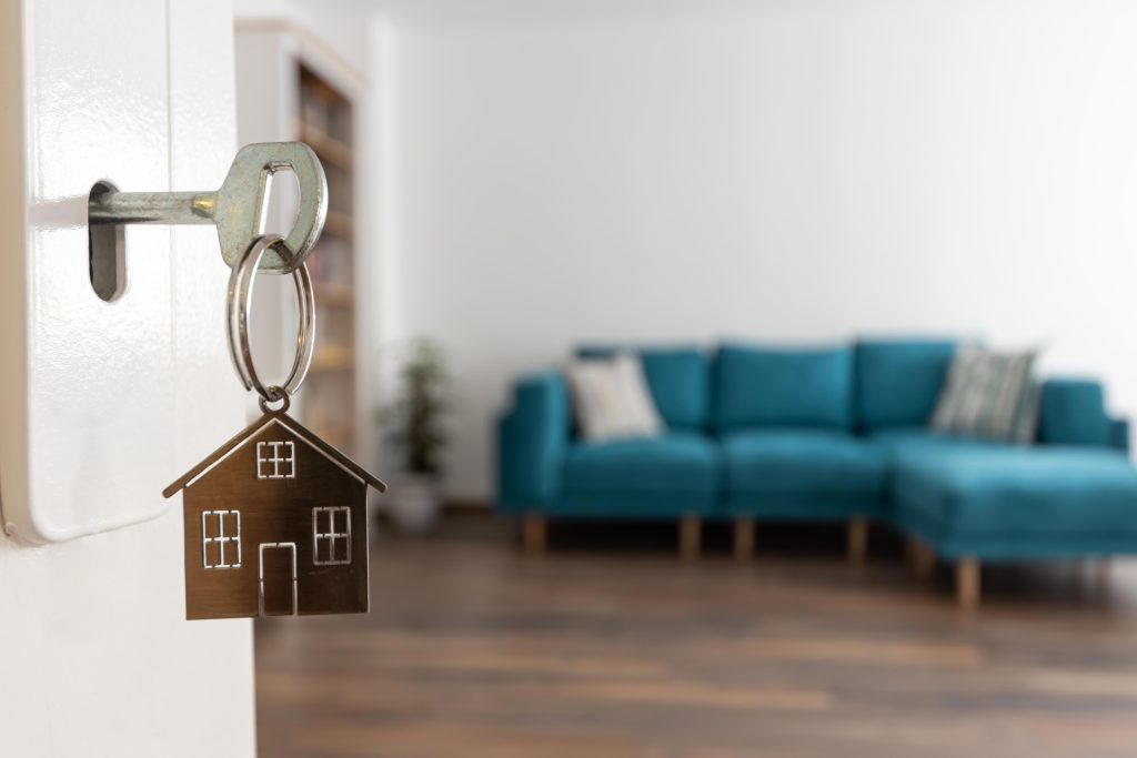Chave com pingente em formato de casa na porta de um imóvel, simbolizando nova moradia e valorização imobiliária.