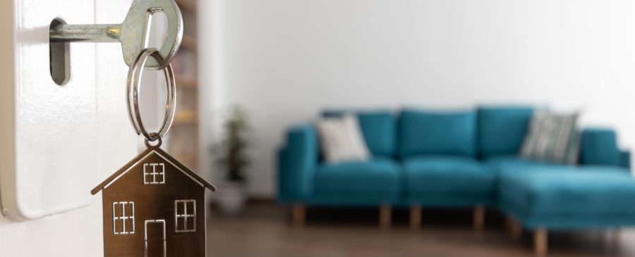 Chave com pingente em formato de casa na porta de um imóvel, simbolizando nova moradia e valorização imobiliária.